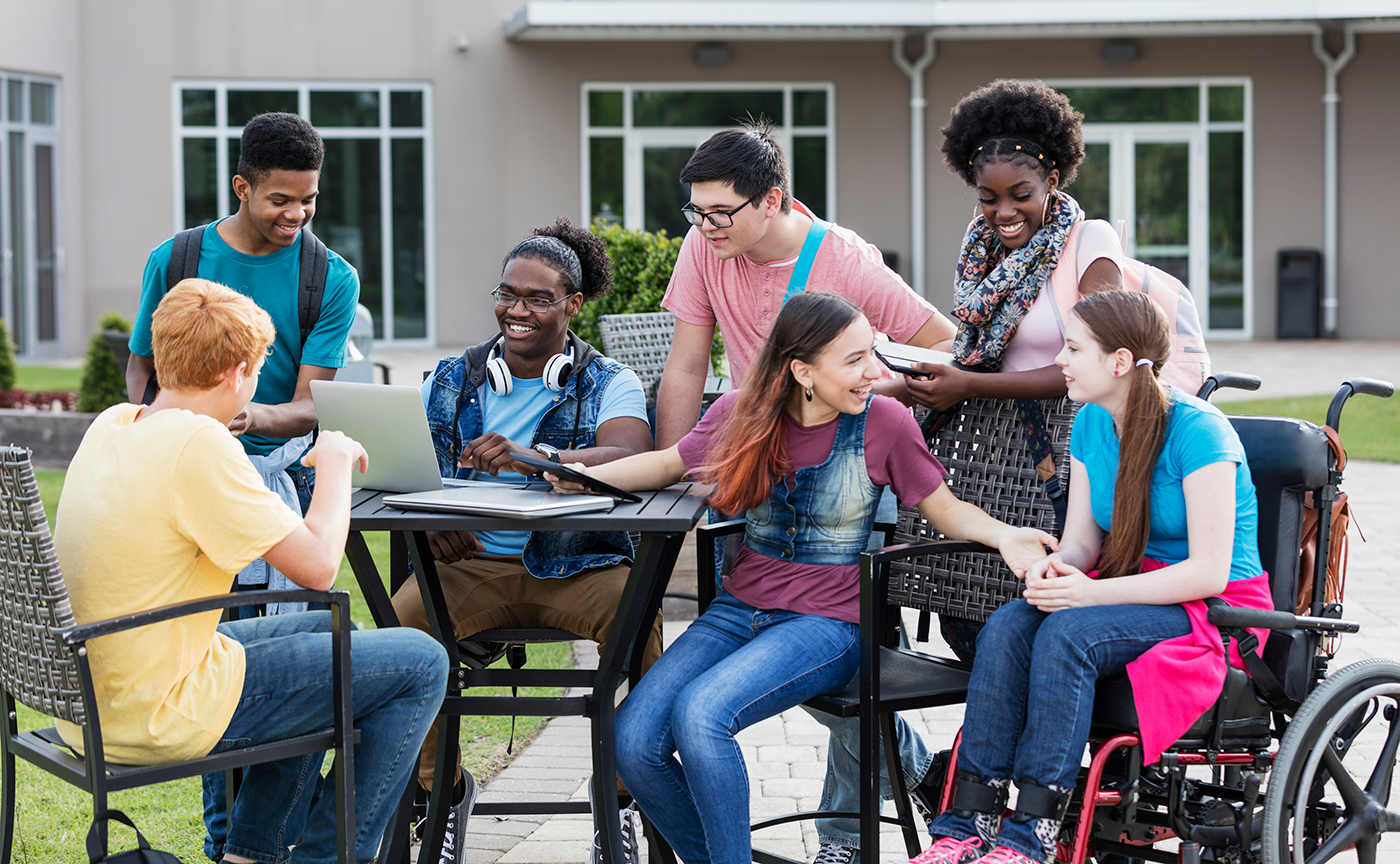 A multi-ethnic group of students gather around a table outdoors