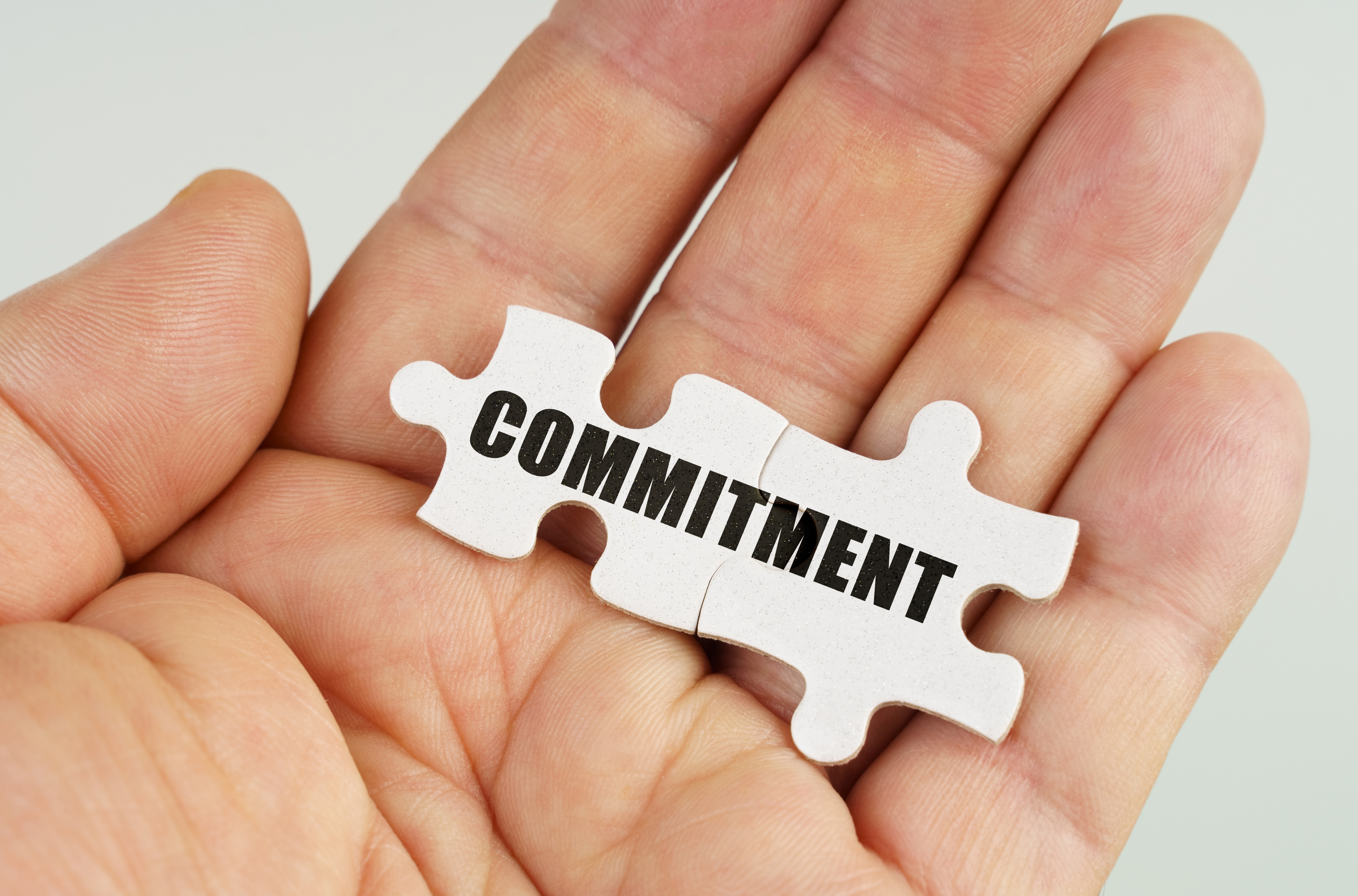 Image with a hand holding two white puzzle pieces that say committment