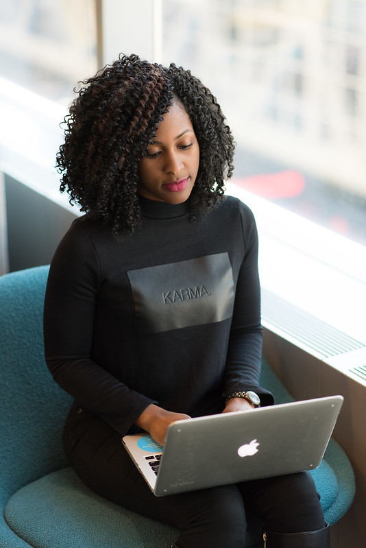 A Black woman with an afro types on their laptop. Attribution: #WOCinTech Chat 