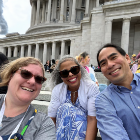 Three people smiling while sitting on the state Capitol steps.