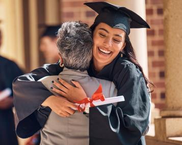 Photo of people in a brick hallway. A smiling female graduate hugging an older relative.