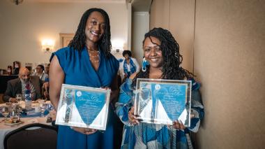Two Black women wearing blue dresses and holding awards smile at the camera. Megan Matthews, Office of Equity Director, and TraeAnna Holiday, Office of Equity Communications Director at the Zeta Phi Beta Sorority Awards Dinner.