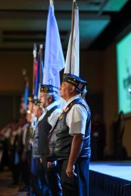 A line of indigenous veterans stand holding various flags as if they were leading a salute.