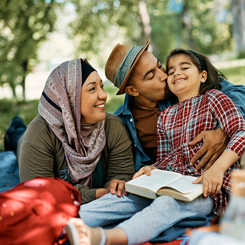 Two parents laugh with their child in a park.