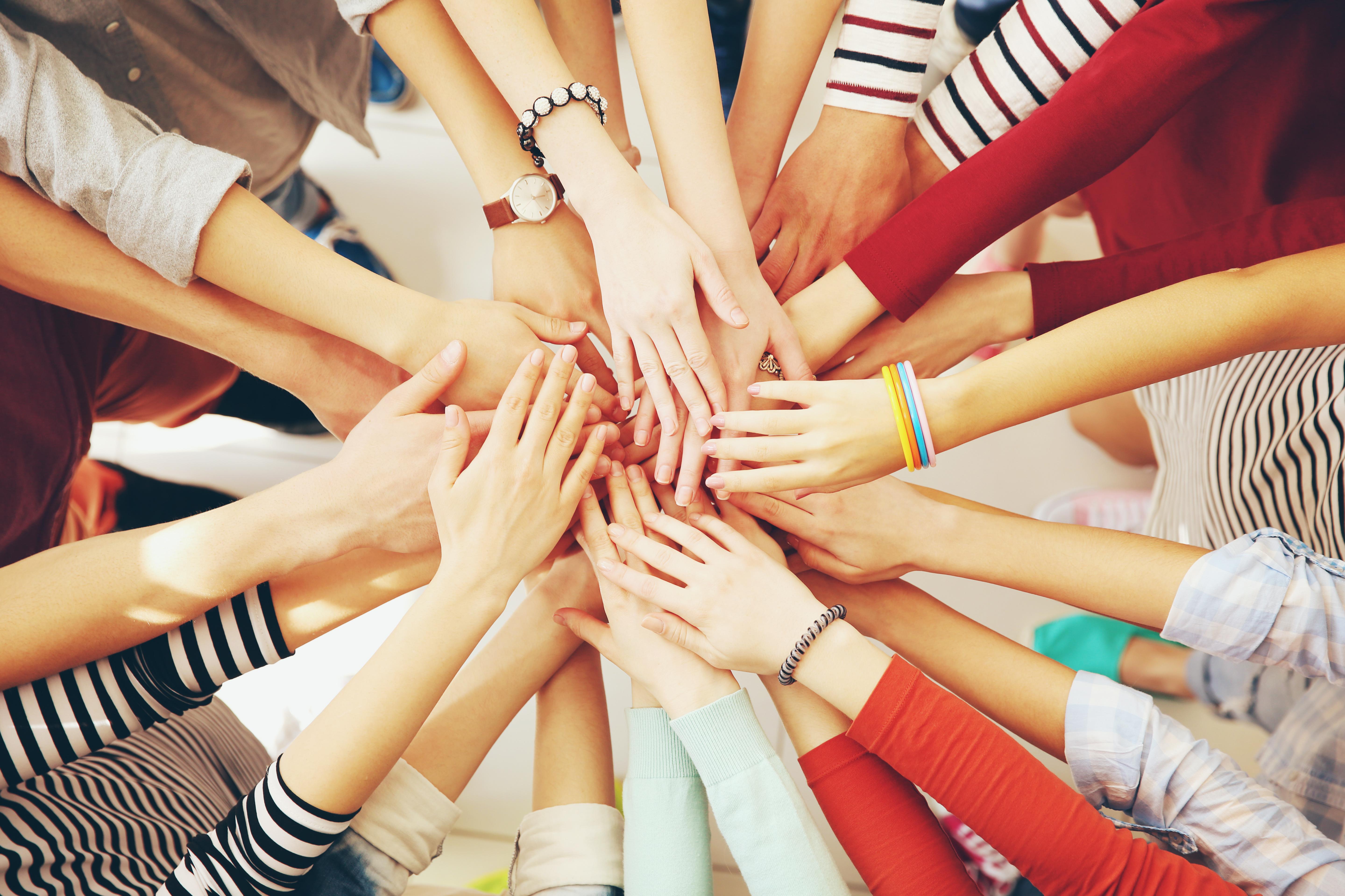 Group of hands from people of multiple races piled on top of each other to symbolize cooperation.  