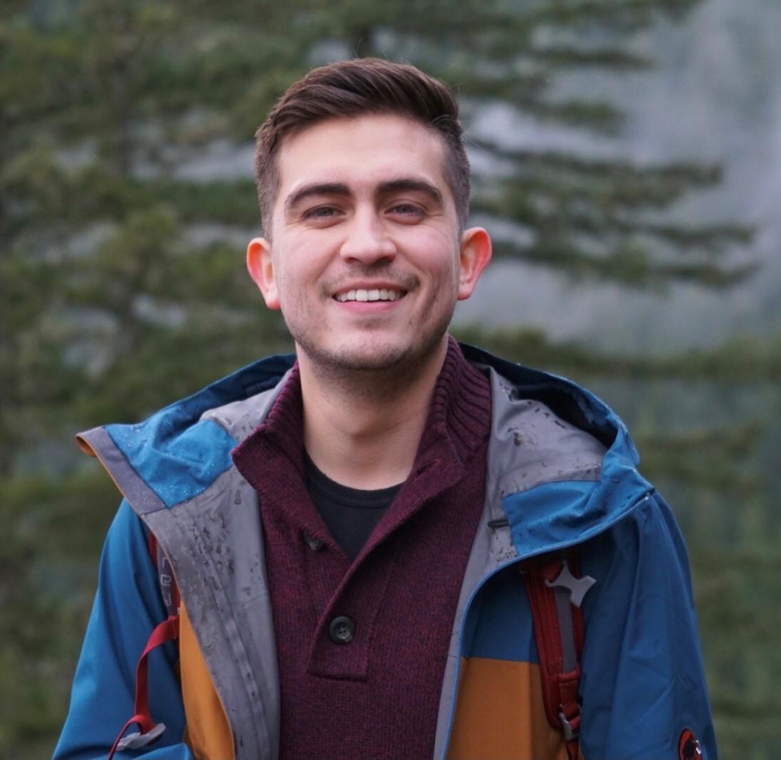 A photo of this episode's host Omar Santana-Gomez. He is standing outside, smiling at the camera while wearing a coat